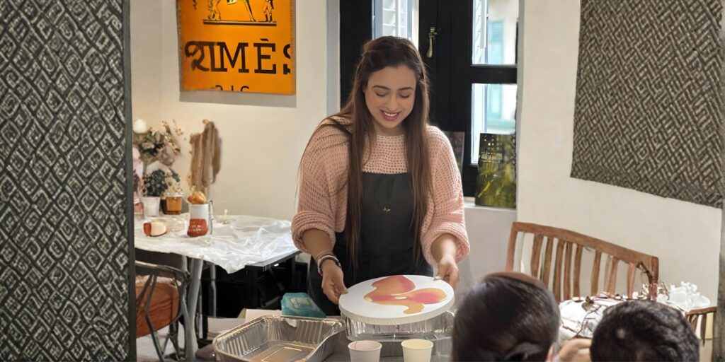 Anit Kaur Art Empowers Women Through Healing A woman smiling as she presents a painted circular artwork to others in a warm, creative environment.