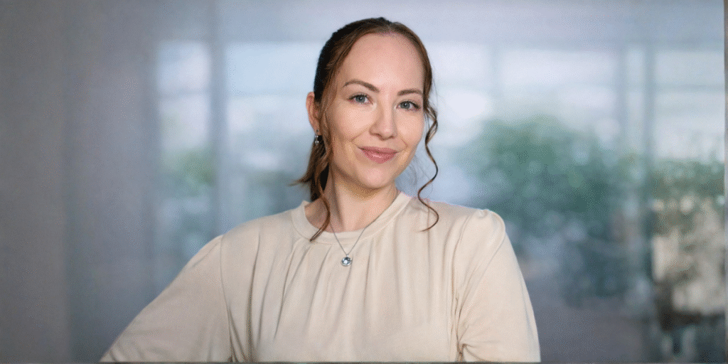 Professional woman smiling in beige blouse with blurred office background.