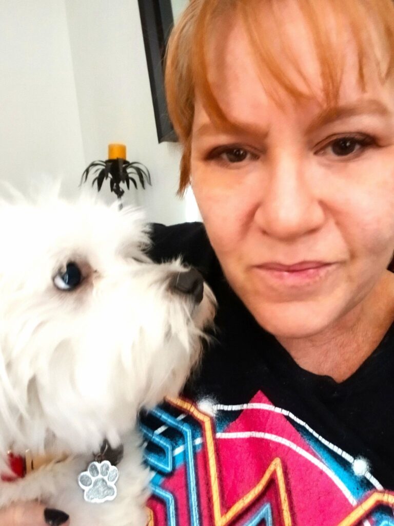 Woman posing indoors beside a small white dog wearing a paw-shaped tag, both looking toward the camera.