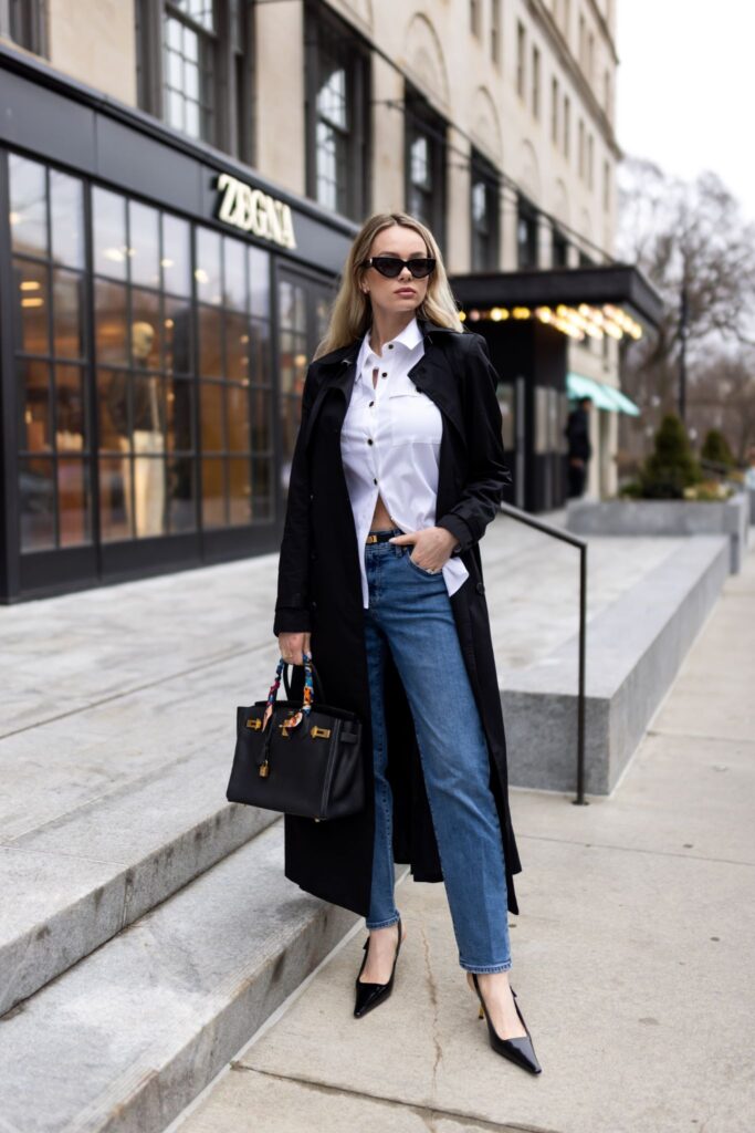 Ksenia Putintseva in black trench coat, white shirt, and jeans walking downtown with handbag, showcasing professional style.