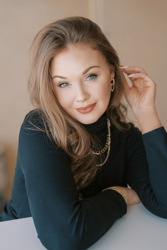 Portrait of interior designer Ursula Carlton wearing black top and gold jewelry, smiling softly indoors.