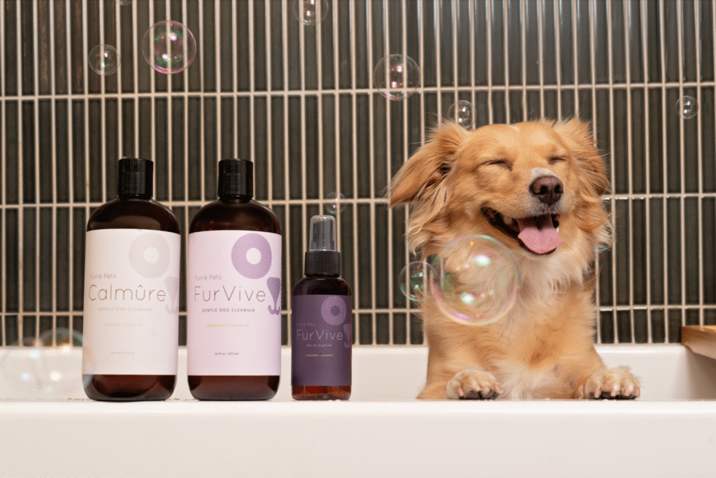Happy dog beside Furré Pets cleansers and pawfum in bath setting with floating bubbles.