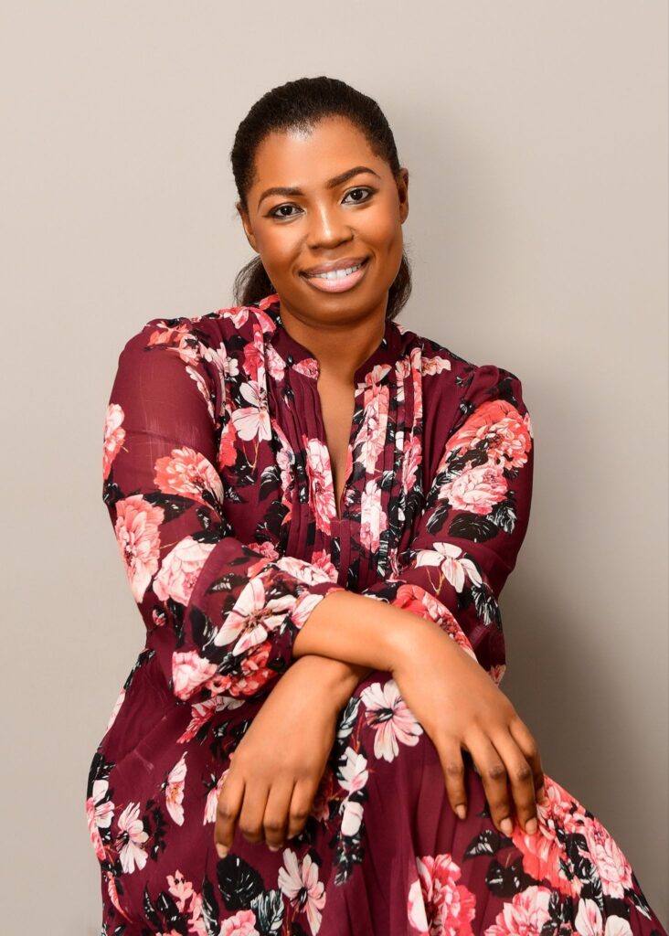 Abigail Owusu posing casually in floral dress against gray backdrop for Hairylin Organics profile.