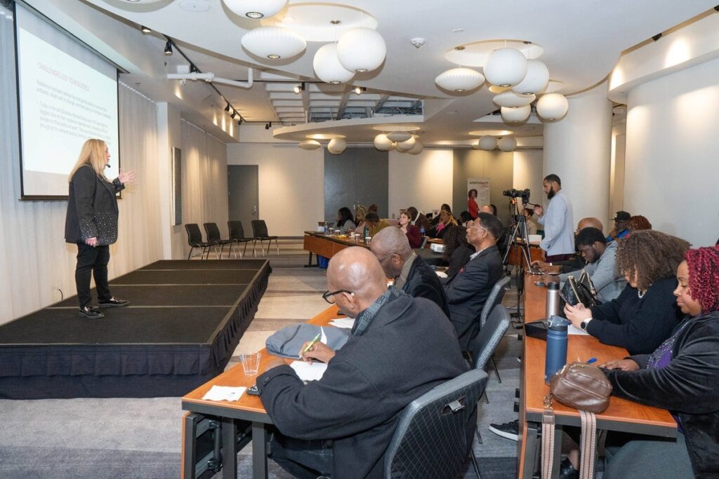 Alicia Pozsony speaking on stage to attendees during a leadership and resilience workshop.