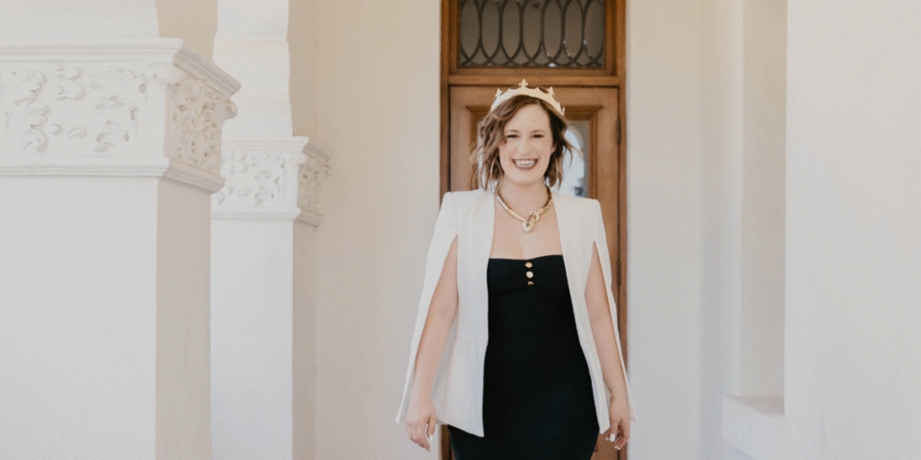 Kimberly Spencer walking confidently through an archway wearing a white blazer and crown.
