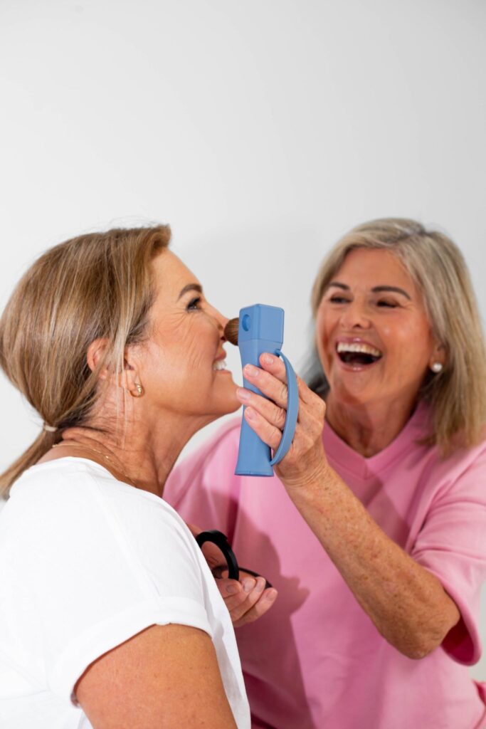 Two women laughing while demonstrating Flexxi Beauty’s accessible makeup brush during makeup application.