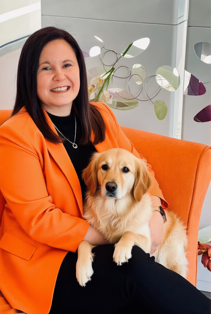 Tracey Franco seated in an orange chair holding a golden retriever in a modern office setting.