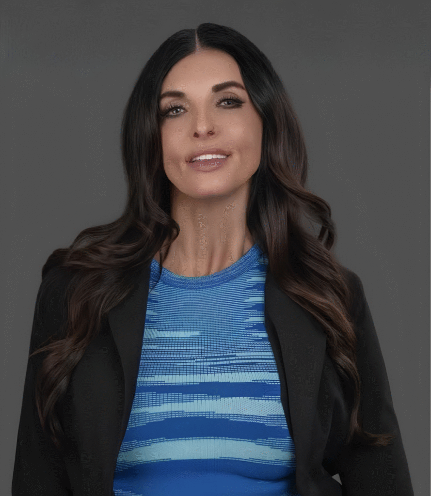 Professional headshot of Candice Noguera wearing a blue patterned top and black blazer against a gray background.