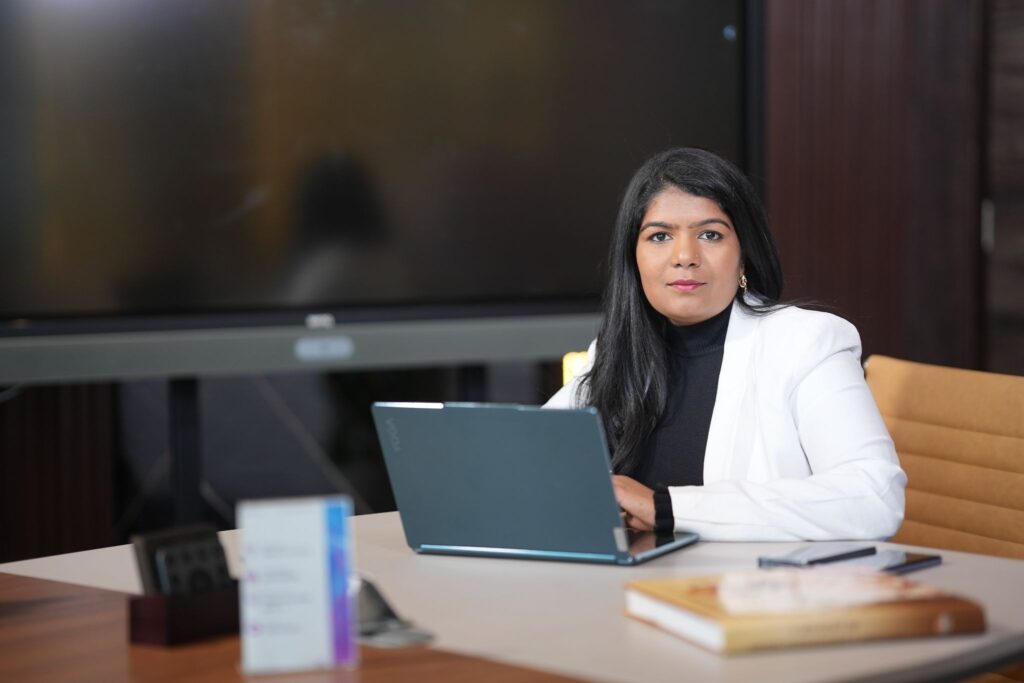 Ashwini Kotaru seated at office desk with laptop, representing global AI leadership and operations.