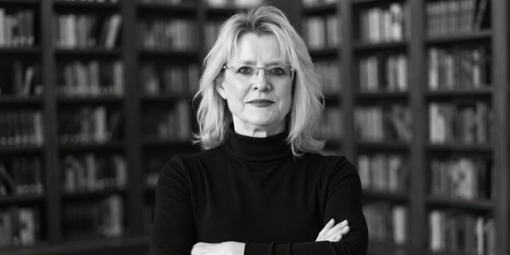 Sandra Griffith Turns Mystery Into A Literary Event Sandra K. Griffith in front of bookshelves with arms crossed.