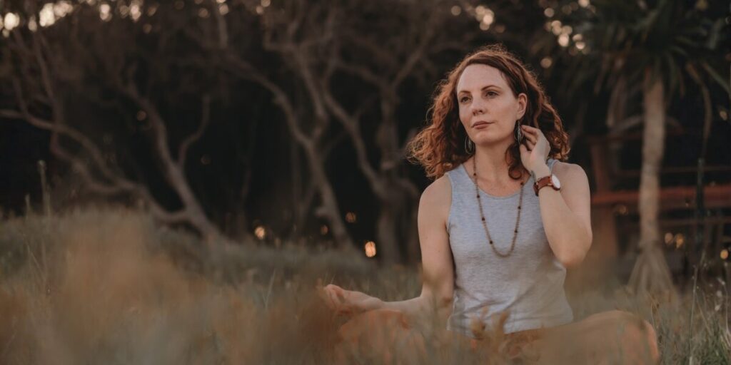 The Hidden Patterns That Shape Your Financial Life Lea Clothier sitting outdoors in meditation with hands resting on her knees.