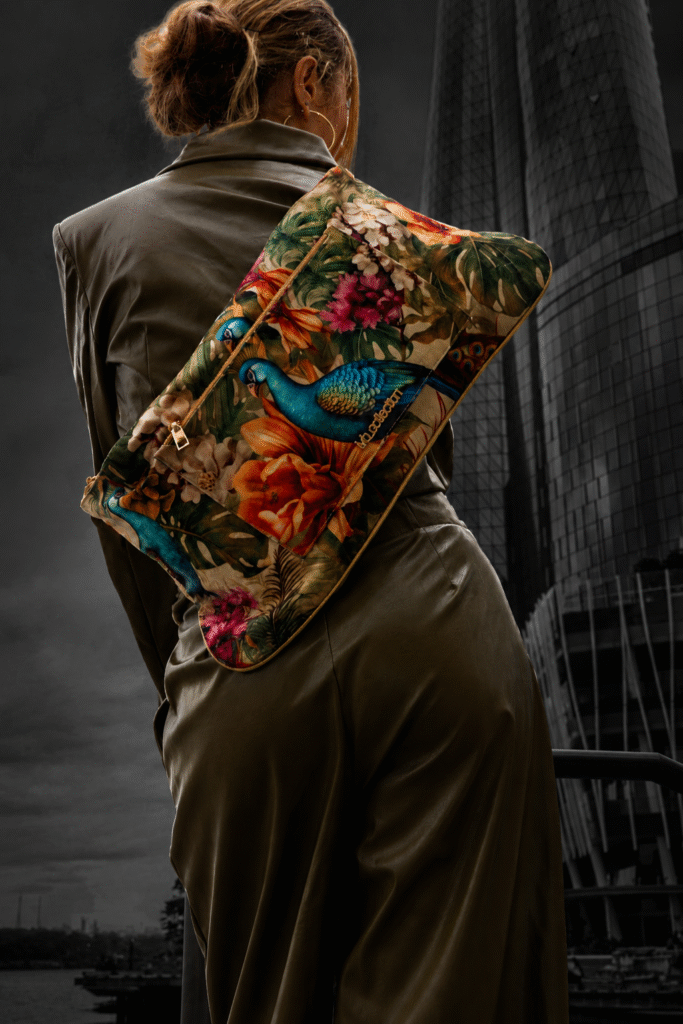 Model carrying floral peacock-print lvb_collection laptop bag over olive leather outfit.