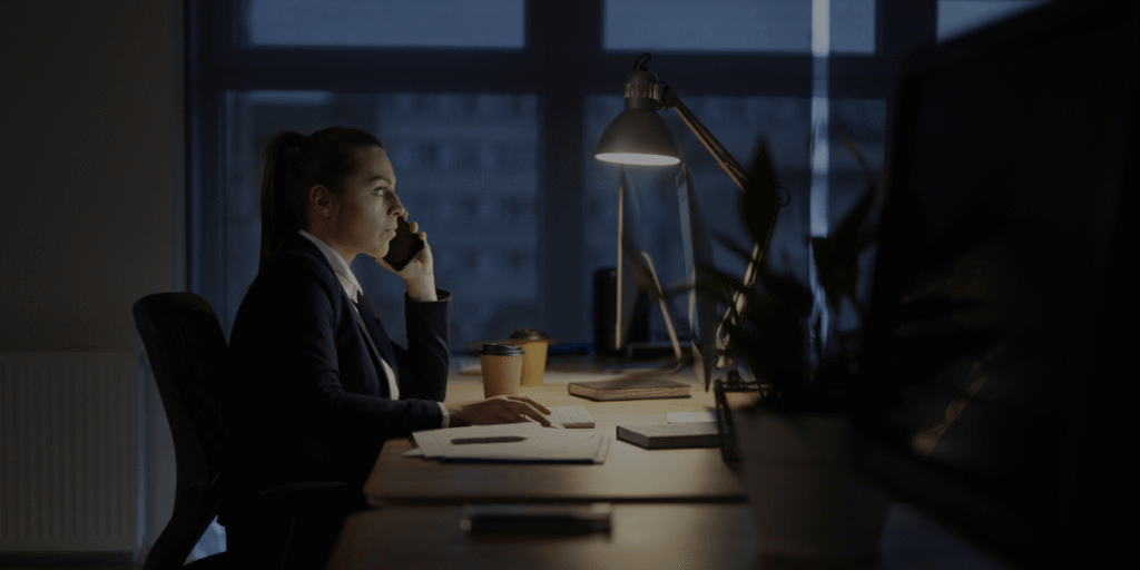 Why Successful Leaders Still Feel Exhausted Business professional working late at a desk while talking on the phone in an office.
