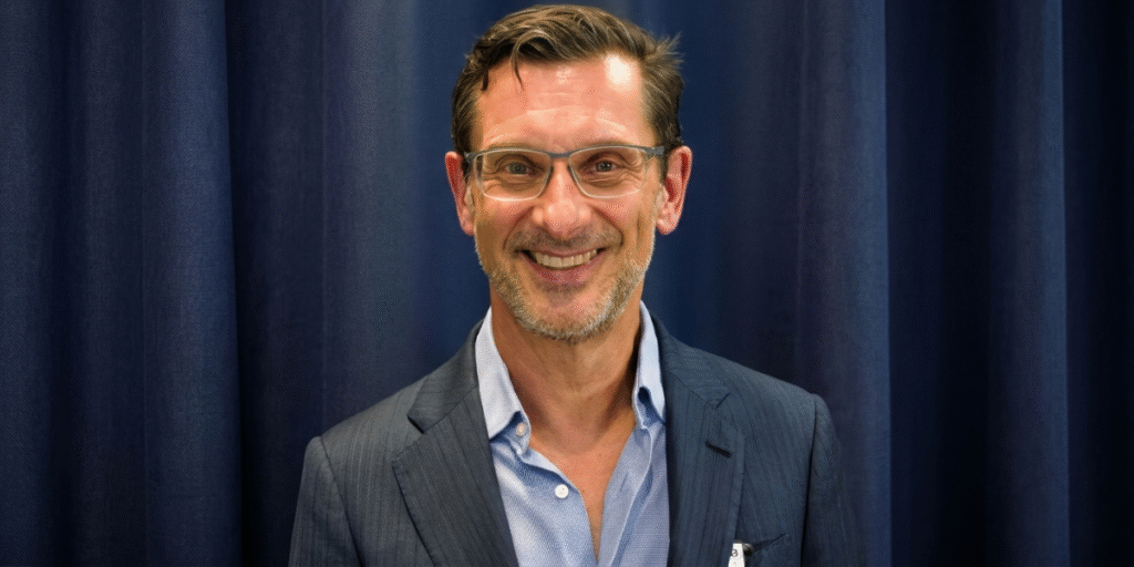 Dr. Mark Kohout smiling in a suit before a dark blue backdrop.