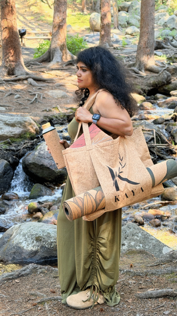 Person carrying a Kaya cork yoga mat, cork tote, and cork water bottle by a forest stream.