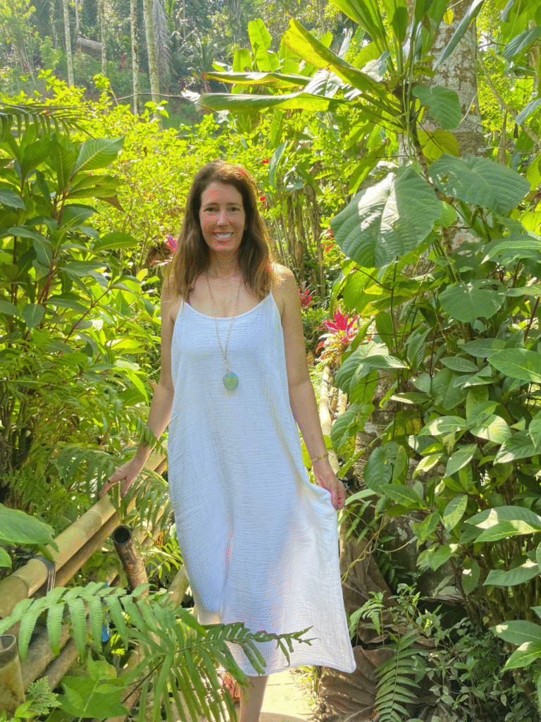 Woman in a white dress standing on a lush tropical garden path surrounded by greenery.