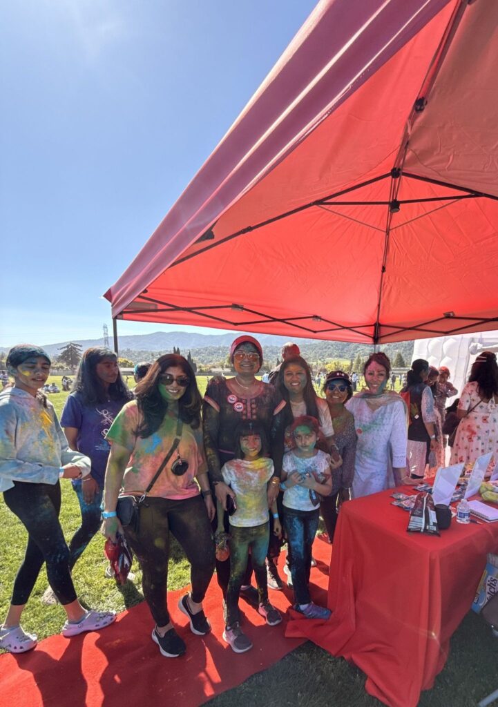 Red Carpet Real Estate Agency team at a community festival booth with families under a red canopy.